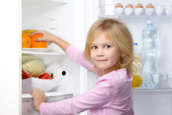 Little girl looking at camera and picking food from fridge