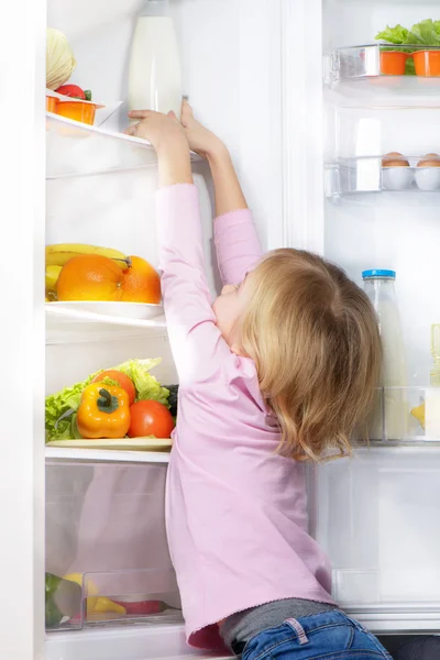 Little cute girl trying to pick food from fridge