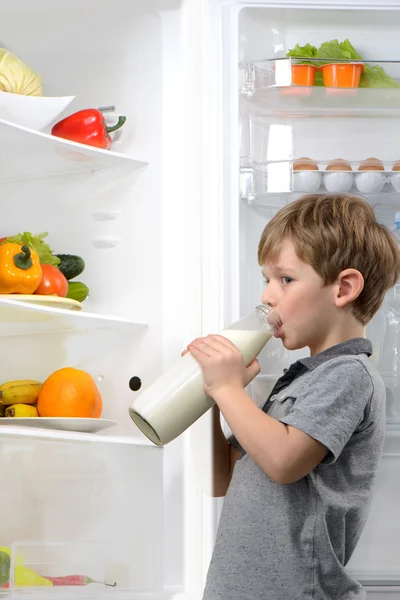 Little boy drinking milk near open fridge