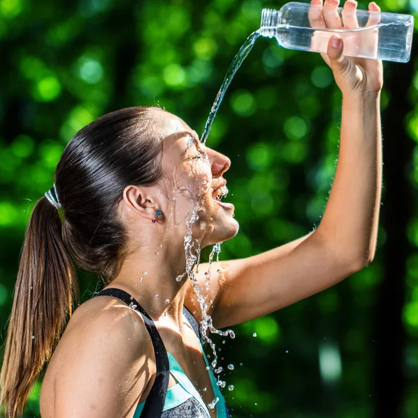 Girl pouring water on face after jog.