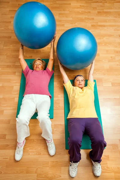 Two senior women doing gym ball exercises on floor.