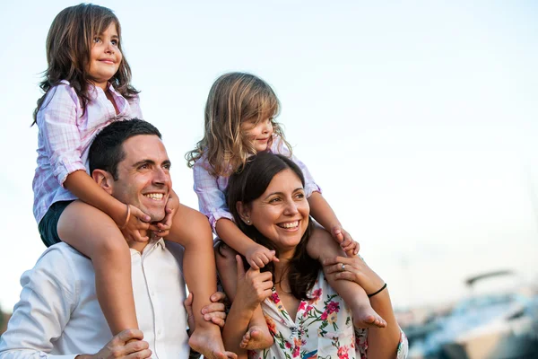 Young couple with kids on shoulders outdoors.