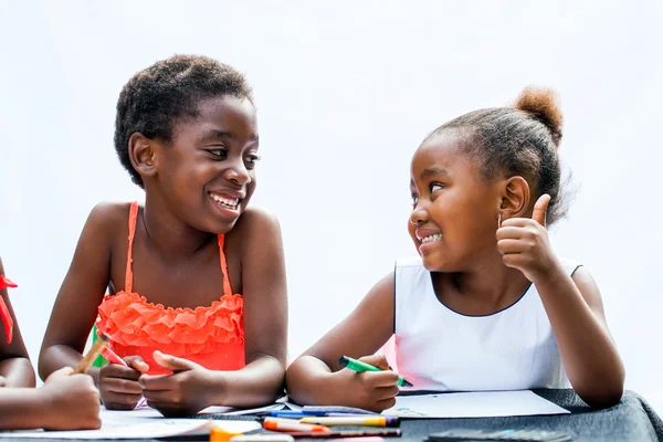 African girl showing thumbs up to friend at desk.