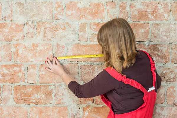 Young woman is measuring a brick wall