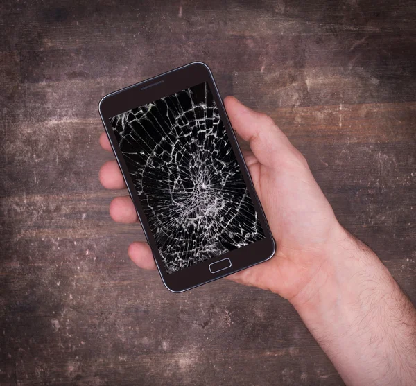 Hand holding a mobile phone with a broken screen