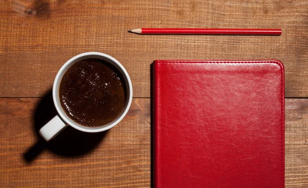 Cup of coffee, a red notebook and a red pencil