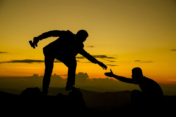 Businessman gived hand for pull team to peak of mountain