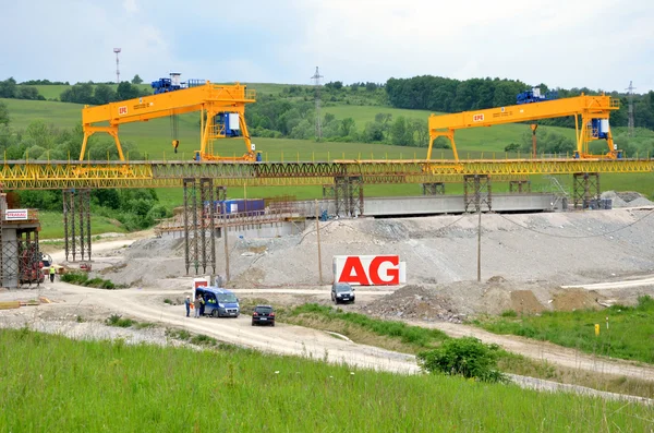 Yellow bridge crane on construction site of slovak D1 highway. Except for the crane there are some workers and cars.