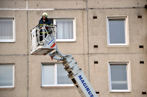 Firefighter uprise into telescopic boom basket of fire truck, block of flats in background