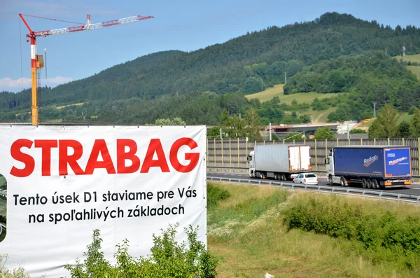 Tower crane working on construction site of slovak D1 highway, billboard of Strabag building company in foreground