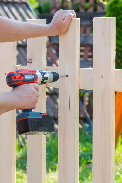 Building a wooden fence with a drill and screw. Close up of his