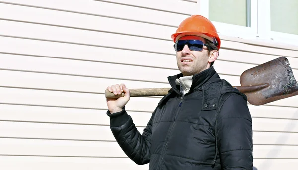The worker in orange hard hat and sunglasses with shovel in his hand