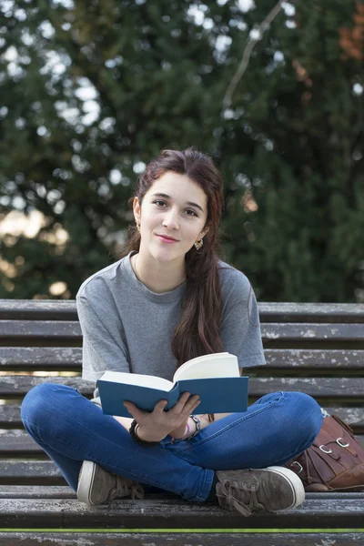 Happiness student sitting on wood bench with blue book, outdoor.