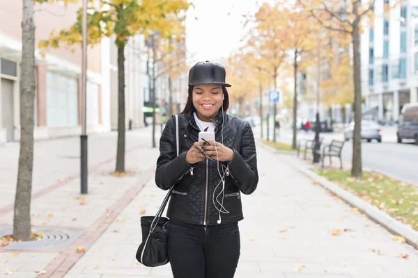 Smiling fashion young woman with headphones listening to music and walking in the street.