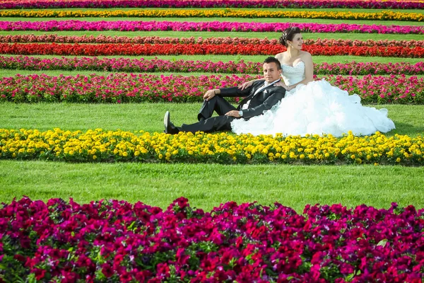Bride and groom sitting on lawn with flowers