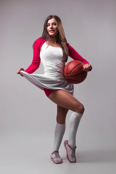 Portrait of young female basketball player passing the ball. Beautiful caucasian woman in sportswear playing basketball on grey background with copyspace