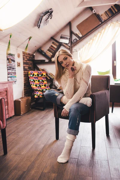 Young woman at home sitting on modern chair in front of window relaxing in her living room