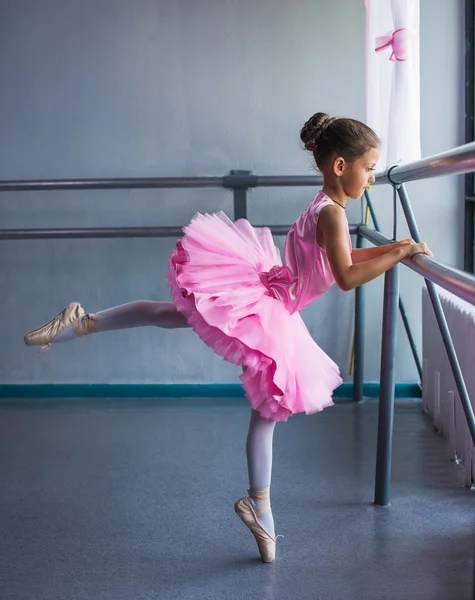 Young ballerina in a pink ballet tutu is dancing in dance class