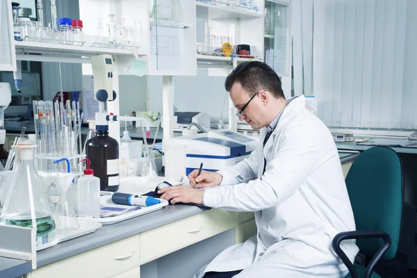 Scentist with pencil writing down observations in laboratory