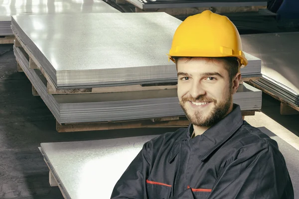 Smiling worker in protective uniform in front of sheet tin metal