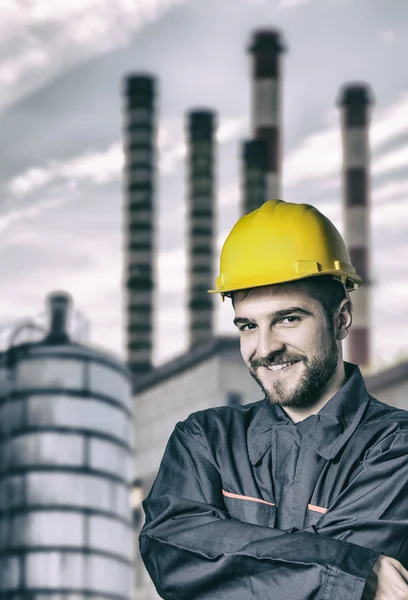 Smiling worker in protective uniform in front of industrial chim