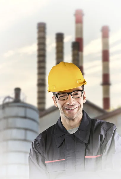 Smiling worker in protective uniform in front of industrial chim