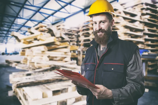 Smiling worker in protective uniform in front of wooden pallets