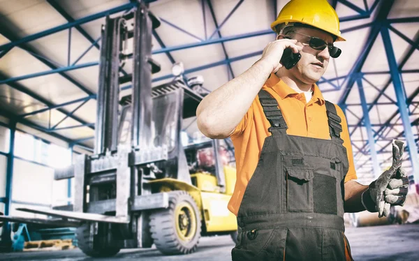 Worker in protective uniform in front of forklift