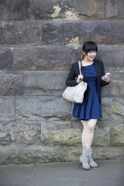 Asian woman using phone leaning against wall