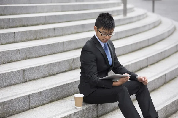 Overhead view of Asian businessman sitting on steps using a tab