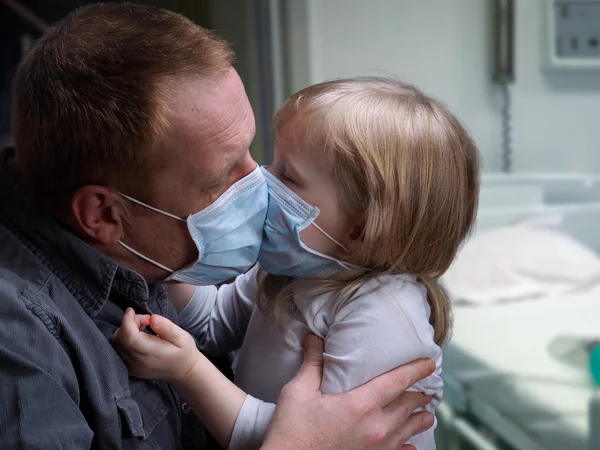 Father kissing daughter through medical mask.