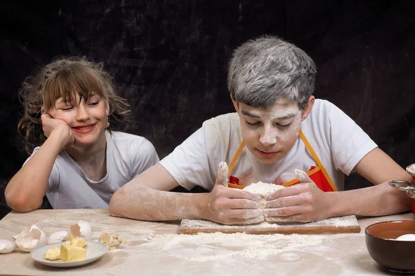 Teens knead the dough. Funny girl and the guy, mired in the flour. Baking Products.