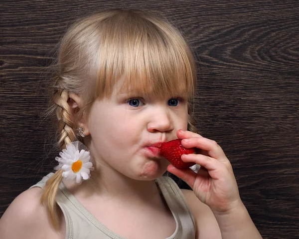 Funny little girl eating a strawberry