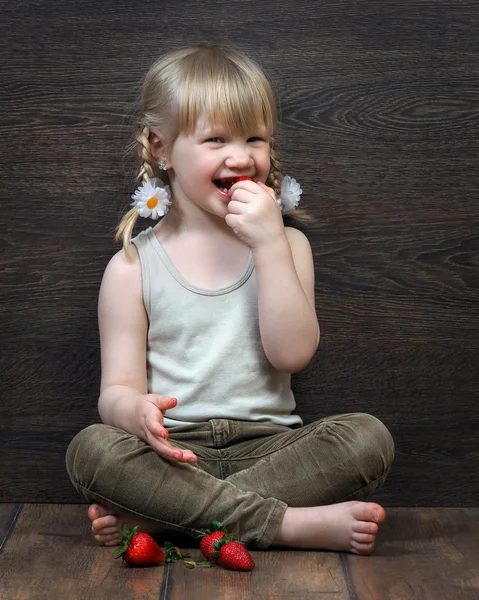 Funny and happy little girl eating a strawberry