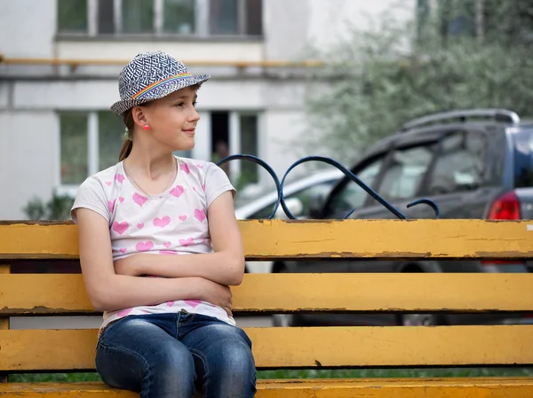 Teenage girl in a hat sitting on a bench near the house