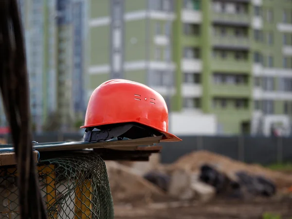 Orange construction helmet lies on a metal structure against a background of construction of fences and buildings - buildings