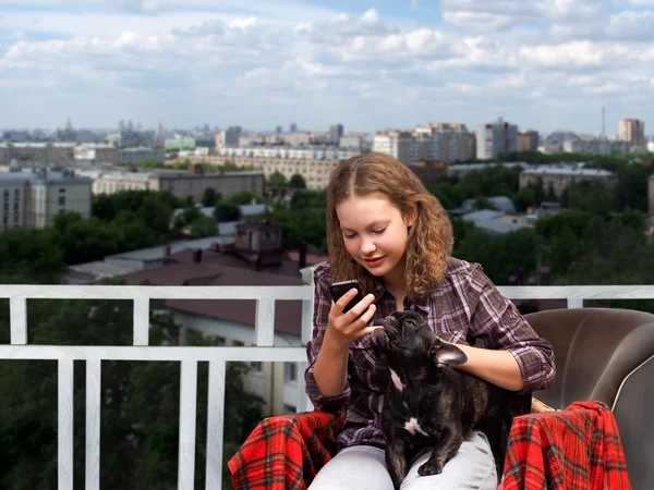 Girl with smart phone and a dog in his arms on the background of the city