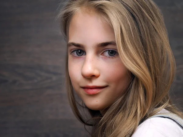 Portrait of a teen girl. Long blond hair, a pretty face. Background dark wooden board