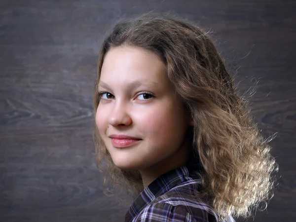 Portrait of a teen girl. A slight smile. Curly hair. Background dark - wood board