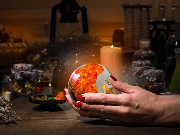 Female hand holding a magical fiery sphere. The golden glow. Flasks, retort for alchemy. Concept - occult, esotericism, spiritualism, calling the spirits and ghosts, underworld