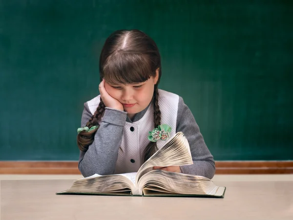 Girl in the classroom reading large textbook. Blackboard. Child obesity full. Portrait of schoolgirl
