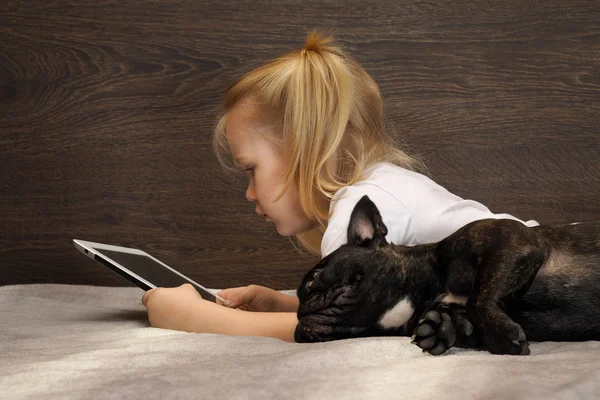 Little girl lies on a tablet and a dog bed