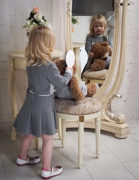 Girl with Teddy unhappy looking in the mirror. The little girl frowns