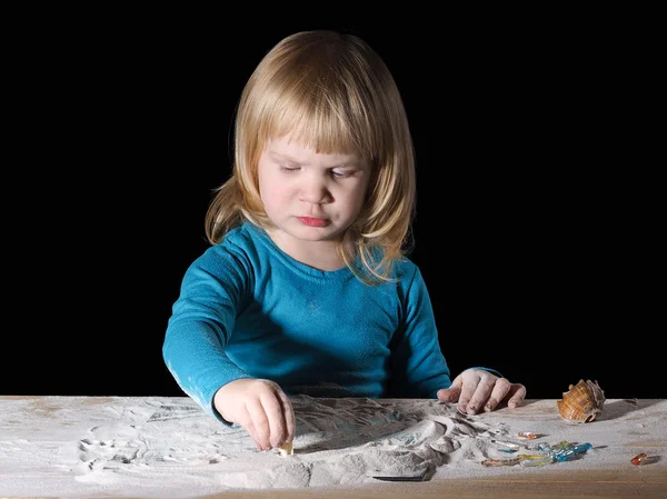 Child playing with sand on the table
