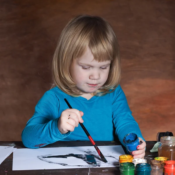 A child paints a black, blue paint and a brush on a piece of paper