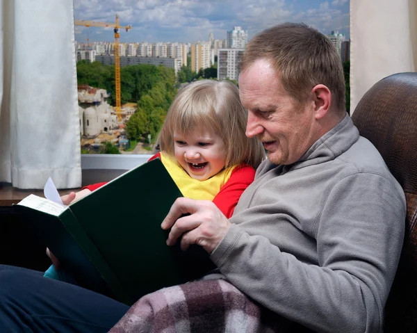 Dad and little daughter reading book. Girl laughing happily. Outside, the city built the house.