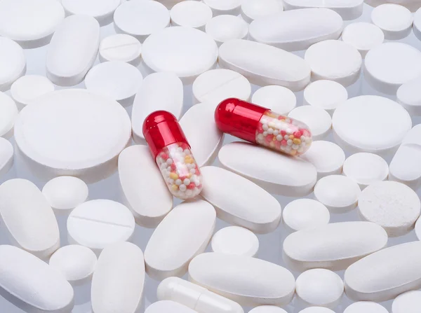 Many white tablets and two red capsules transparent.