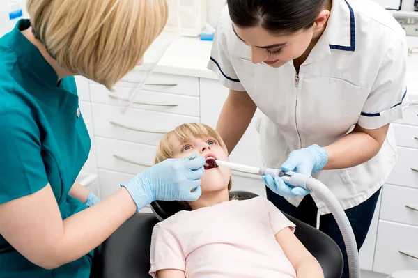 Girl examined by dentist and assistant