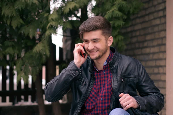 Handsome hipster in leather jacket speaking on the phone outdoor