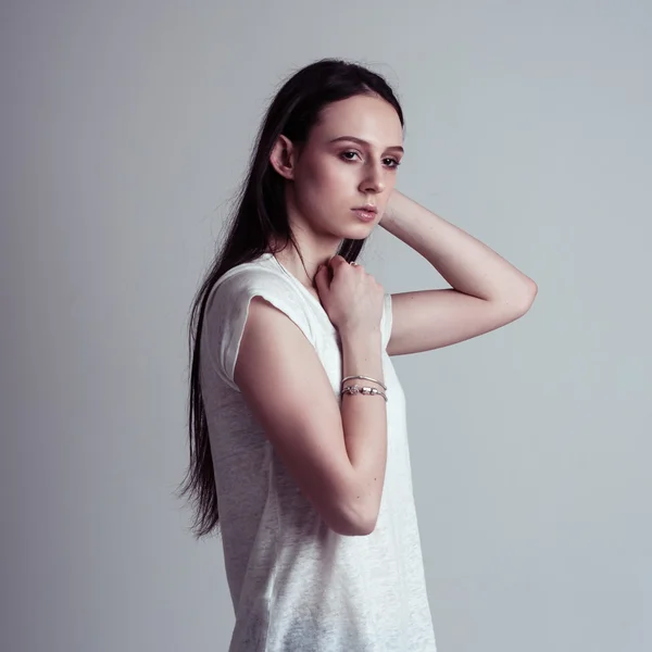 Young brunette girl with long hair. Natural beauty. Isolated on a gray background